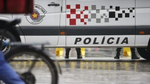 Mulher esfaqueia companheiro em Praia Grande: Viatura da Polícia Militar com palavra POLICIA ao fundo, ocupantes em área de investigação, em contexto de suspeita de crime em Praia Grande.