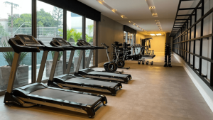 Papo de Síndico: academia com esteiras e equipamentos de musculação em corredor amplo e iluminado, com janelas grandes voltadas para área externa e detalhes do salão