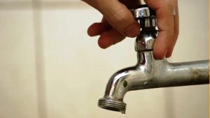 Falta de água em Guarujá: morador segura uma torneira metálica com o registro entreaberto, mostrando interrupção do fornecimento e moradores relatando até seis dias sem água.