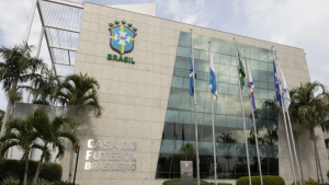 Prédio sede da CBF Brasil com bandeiras ao lado da fachada, em frente a palmeiras; imagem relacionada a CBF novas regras contra antijogo e cera.