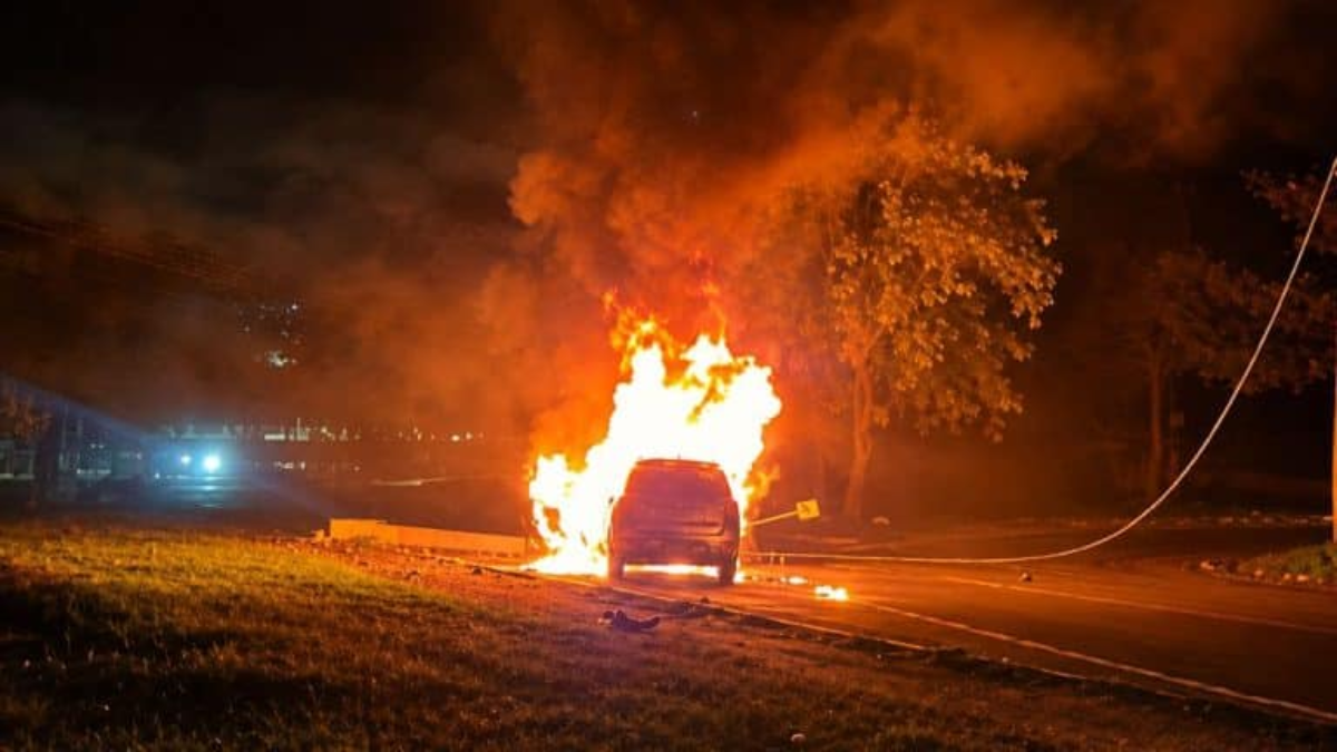 Carro pega fogo em campinas à noite após bater em um poste, com chamas altas e muita fumaça na via, enquanto veículos e iluminação de emergência aparecem ao fundo.