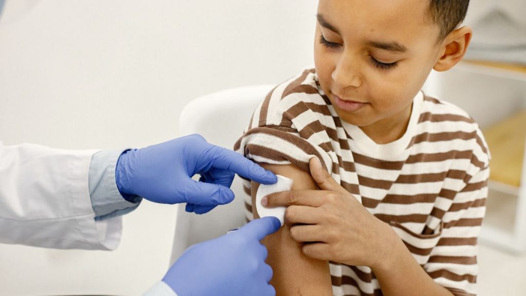 Médico com luvas aplica vacina no braço de uma criança, em ambiente clínico, com foco no procedimento de imunização contra sarampo.