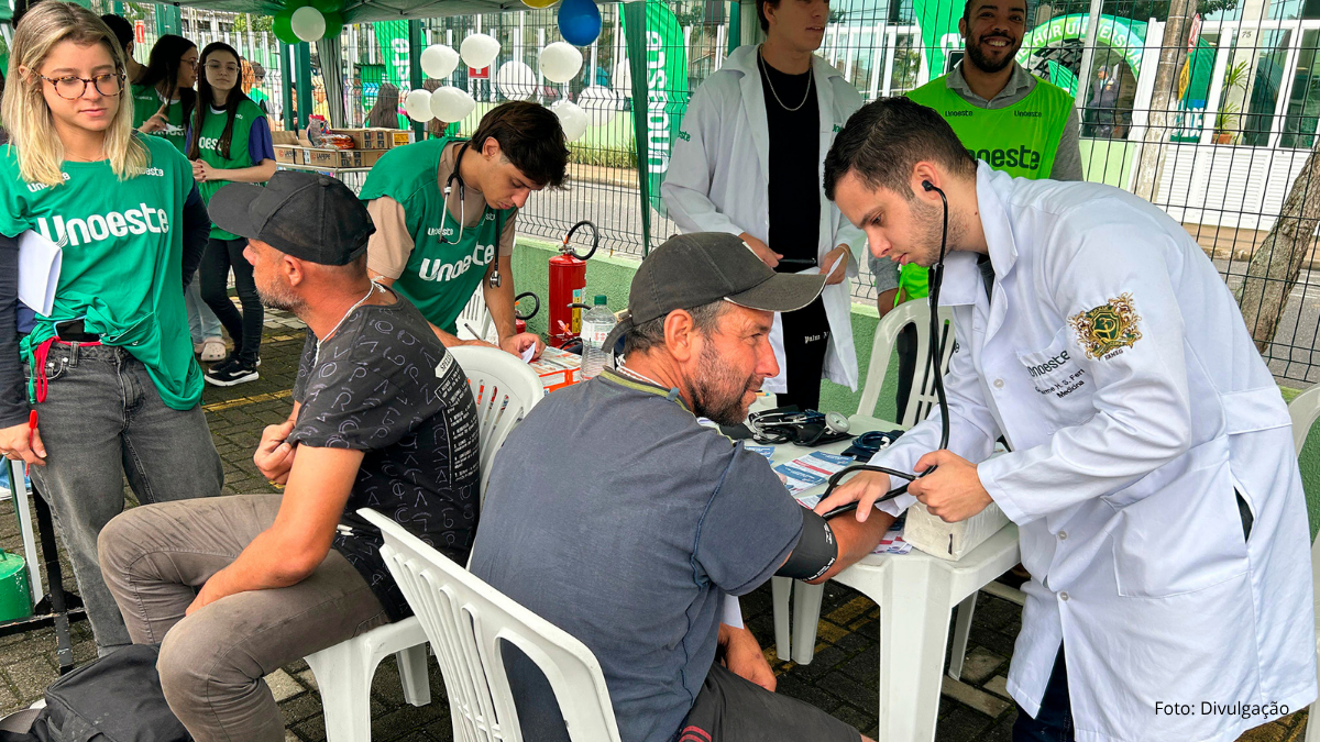 Equipe com profissionais atendendo moradores em estande de serviços gratuitos em Guarujá, com voluntários e participantes conversando e realizando atendimentos ao ar livre.