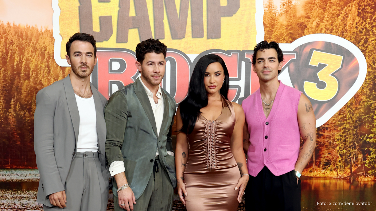 Demi Lovato e Jonas Brothers na première de Camp Rock 3, com quatro artistas posando juntos em frente a um painel promocional do filme.
