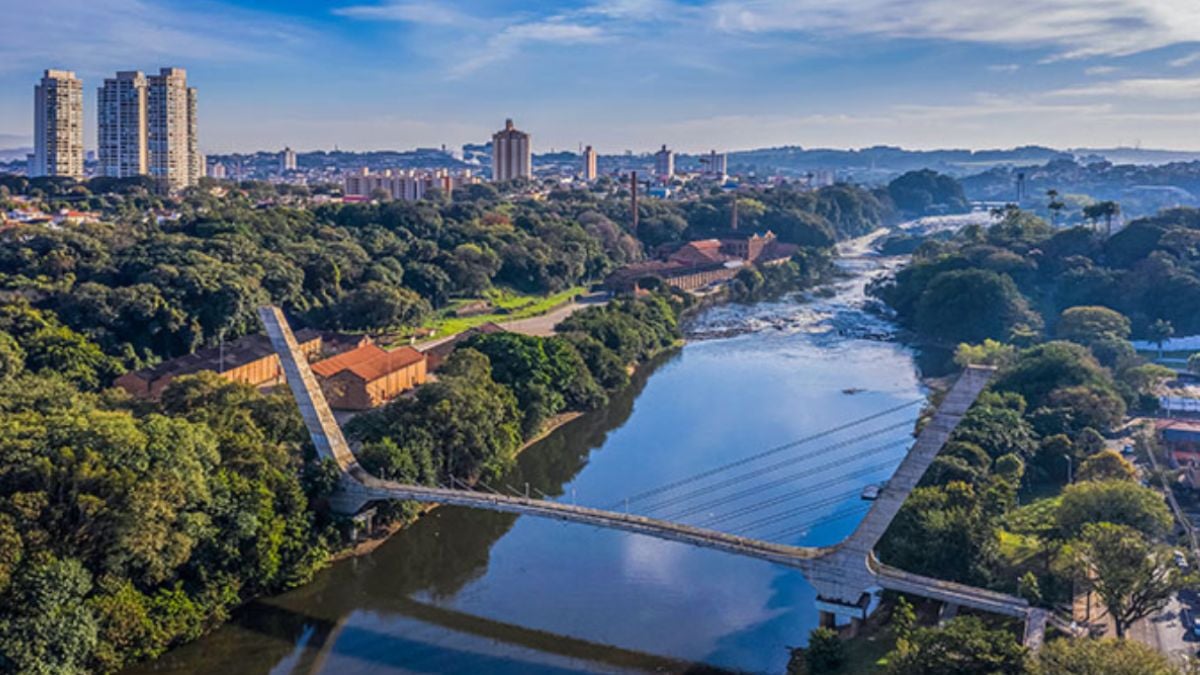 Vista aérea de um rio com ponte e área urbana ao fundo, com vegetação ao redor; a Câmara de Piracicaba cobra dados sobre delação e acordo de leniência da Aegea.