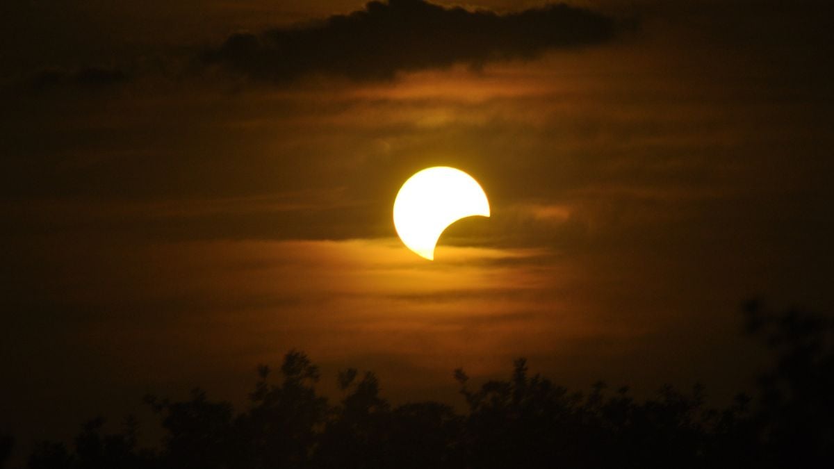 Eclipse solar com o Sol parcialmente encoberto, visto no céu ao entardecer, com nuvens ao fundo; imagem de referência para transmissão ao vivo no Brasil.