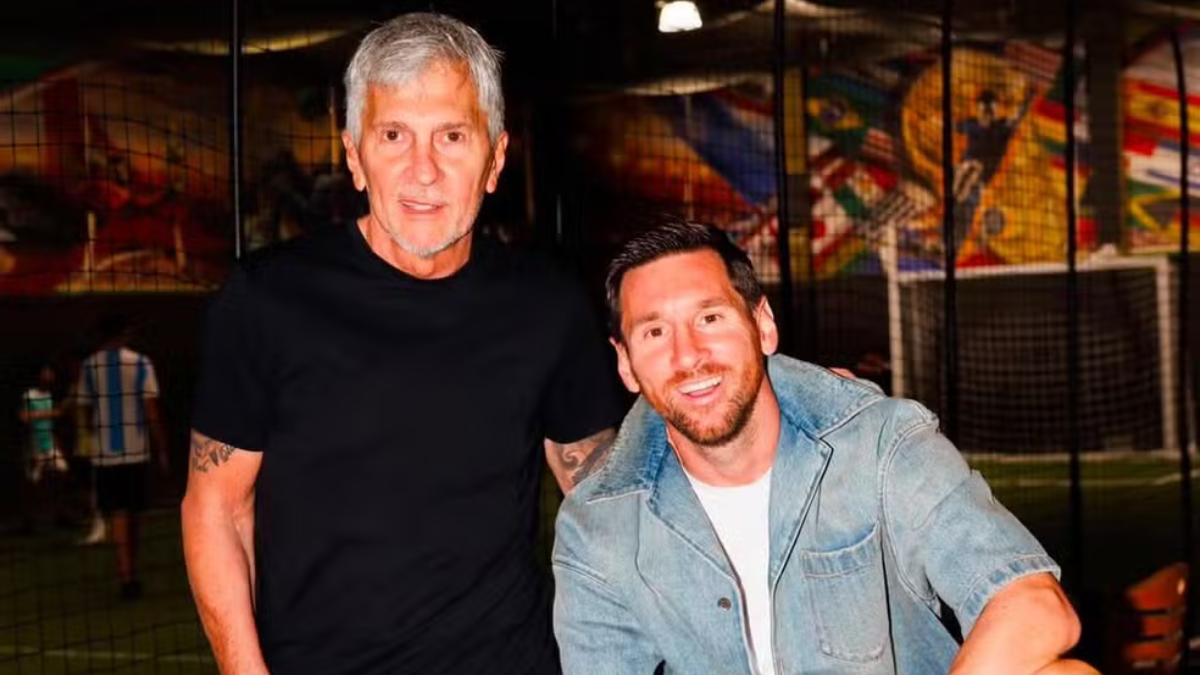 Messi aparece ao lado de um homem mais velho em uma foto noturna, posando sorridente em ambiente externo com iluminação baixa.