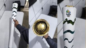 Tocha Olímpica Rio 2016 branca com detalhes verdes e dourados, vista em sequência durante recuperação após furto em Guarujá, cerca de cinco anos depois.