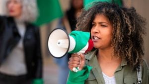 Eleições 2026: mulher segura megafone verde e branco, em ambiente institucional, em referência ao início da propaganda eleitoral no domingo (16), com apelo político