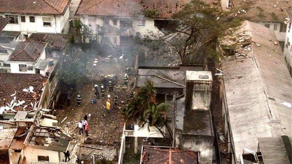 Cena aérea de resgate em local de acidente com destroços e equipes trabalhando ao redor de um jato, cenário após a morte de Eduardo Campos, tema com 12 anos sem conclusão.