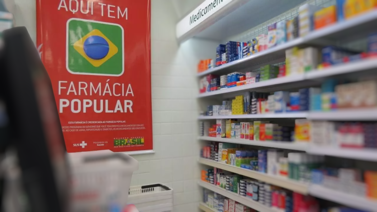 Cartaz do Governo com o logotipo “Farmácia Popular” ao lado de prateleiras com medicamentos em uma farmácia, ilustrando novas medidas do Programa Farmácia Popular.
