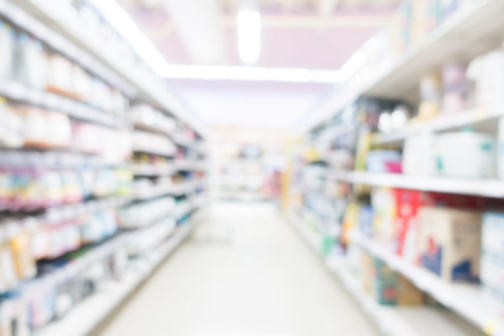 Corredor de farmácia com prateleiras de medicamentos, iluminação suave e imagem desfocada, sugerindo inovação e serviços da Farmácia Popular com ferramentas digitais no atendimento.