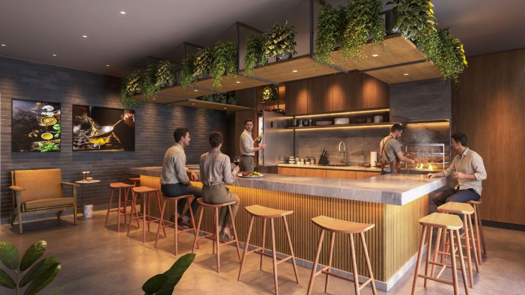 Área de lazer interna com bar, bancos altos de madeira e iluminação quente, com pessoas conversando, em um projeto de empreendimento da Construtora Macuco. Gran Canal Residence em Santos.