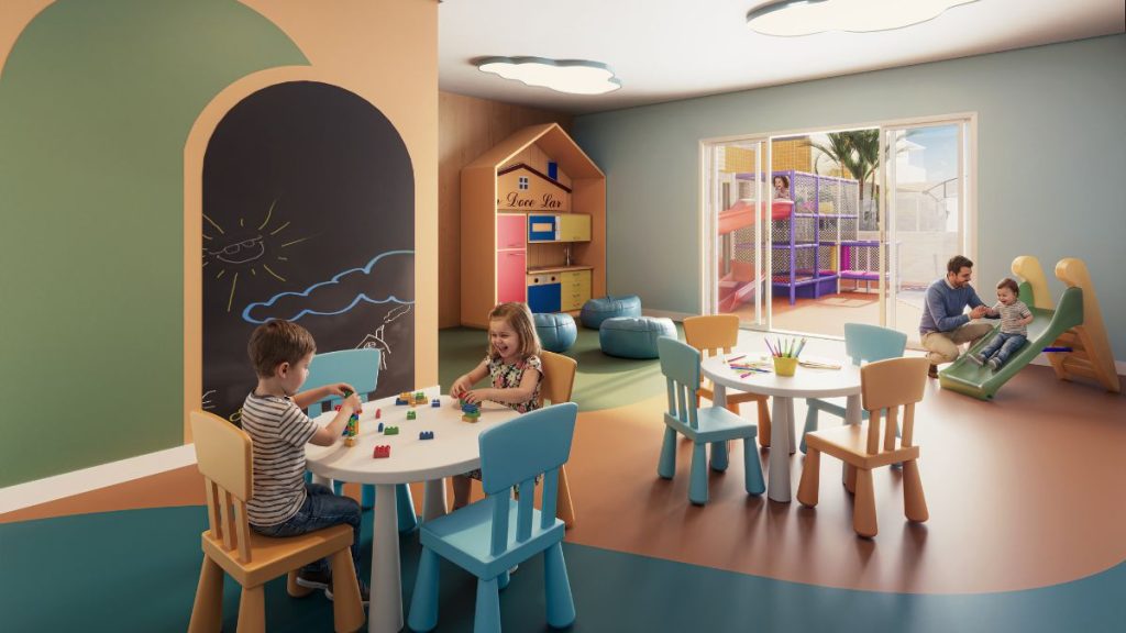 Sala infantil decorada com área de brinquedos, mesas e cadeiras coloridas, com crianças brincando e família no ambiente interno do empreendimento Gran Canal Residence em Santos.