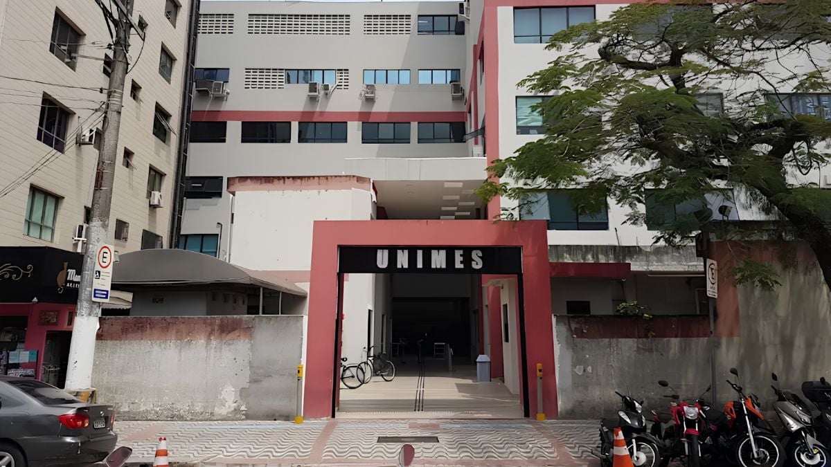 Unimes fraude de títulos: Prédio da Universidade UNIMES no litoral de São Paulo, com entrada e fachada ao ar livre, destacando o nome UNIMES diante de carros e bicicletas estacionados.