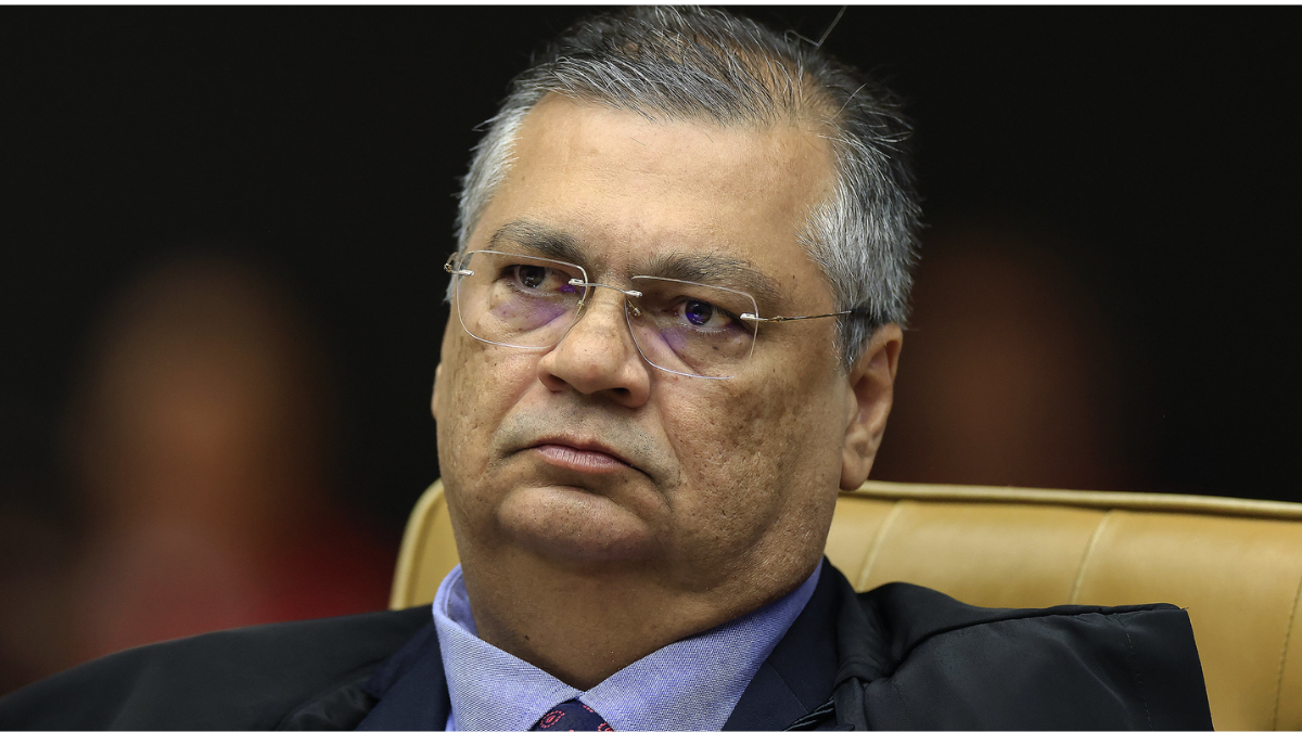 STF: Flávio Dino reage em entrevista no plenário, com expressão séria, usando óculos e toga, enquanto discursa sobre operação e cita “distorção monumental”.