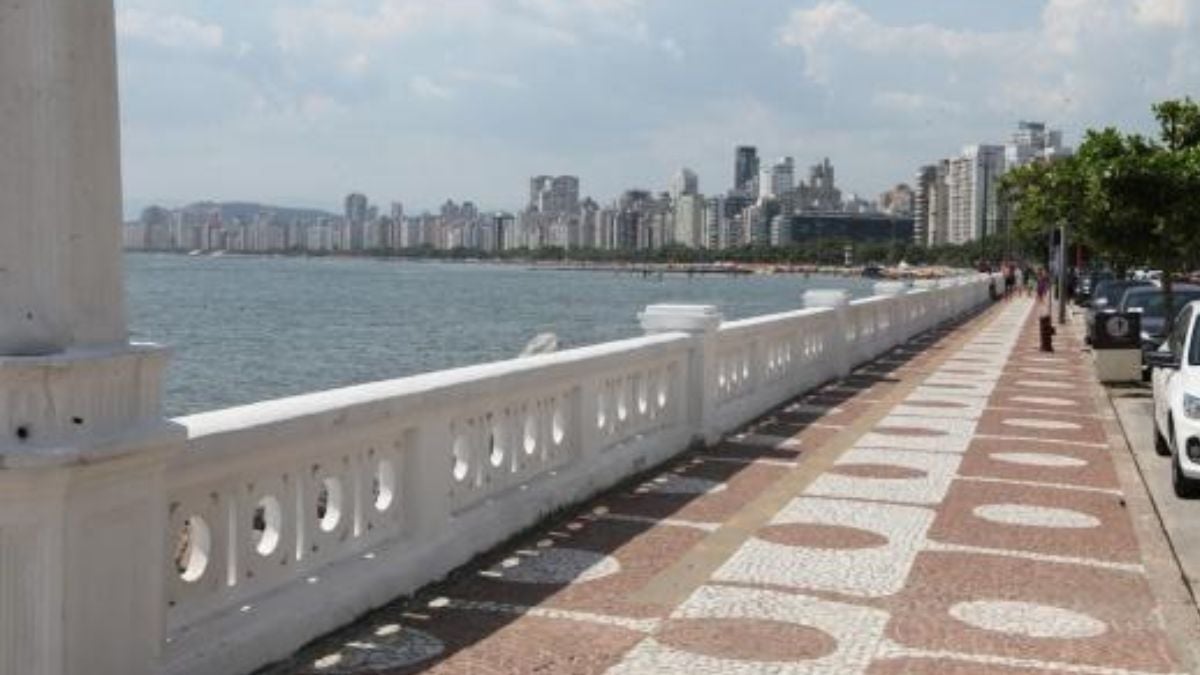Mureta da Ponta da Praia: Vista do calçadão à beira-mar com mureta branca e faixas de piso, ao lado da água e do skyline de prédios ao fundo.