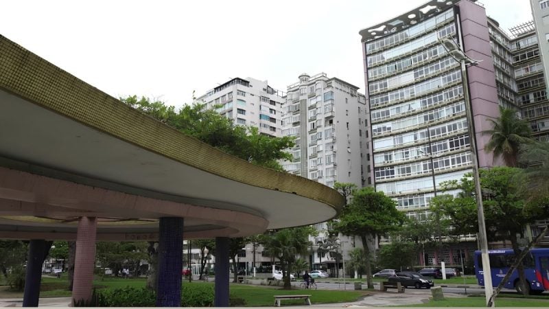 Prédio e área externa na cidade de Santos, com estrutura de segurança e viaturas ao fundo, em cena relacionada a suspeita de crimes sexuais contra mulheres e adolescentes envolvendo homem preso ao lado de adolescente.