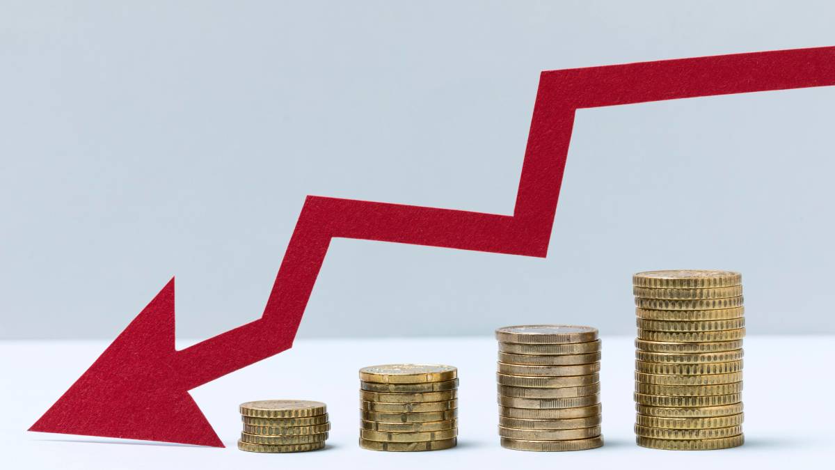 Imagem com moedas empilhadas e uma seta vermelha apontando para baixo, sugerindo sinais de falência e risco financeiro de empresas em crise.