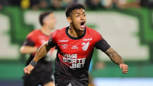 Léo Derik em partida pelo Athletico, usando uniforme vermelho e preto com logos do clube e comemorando em campo, com gramado ao fundo, imagem que acompanha notícia de condenação a 13 anos por estupros.
