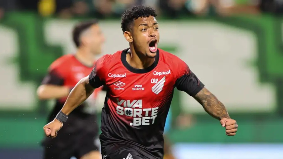 Léo Derik em partida pelo Athletico, usando uniforme vermelho e preto com logos do clube e comemorando em campo, com gramado ao fundo, imagem que acompanha notícia de condenação a 13 anos por estupros.
