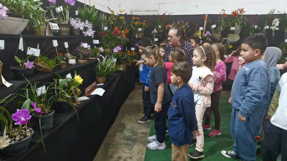 Feira AgroUrbana de Americana: Crianças visitam feira em Americana com exposição e venda de orquídeas, cercadas por vasos e flores em bancadas durante setembro.