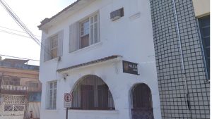 Prédio da Polícia Civil em São Vicente, com fachada branca e janelas em grade, visto em reportagem sobre a situação de Grávida é agredida em São Vicente, de três meses.