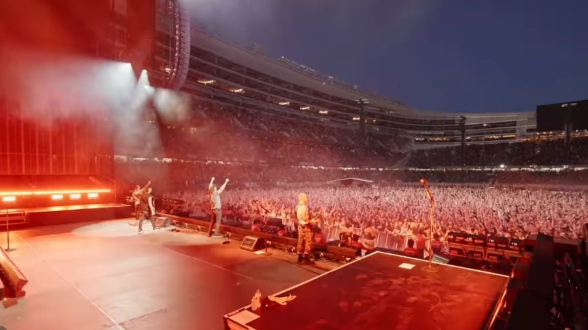 Show System of a Down no Brasil: Palco com banda tocando em um grande estádio lotado, com fumaça e luzes durante um show; System of a Down fará show no Brasil em 2027, veja data e ingressos.