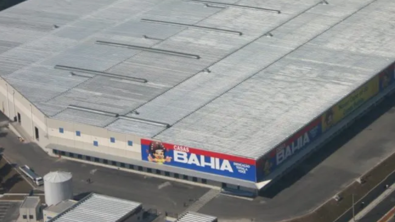 Foto aérea do prédio e da fachada do Centro de Distribuição da Casas Bahia, com grande faixa “CASAS BAHIA” no topo do galpão, sugerindo tema de Recuperação judicial Casas Bahia no varejo.