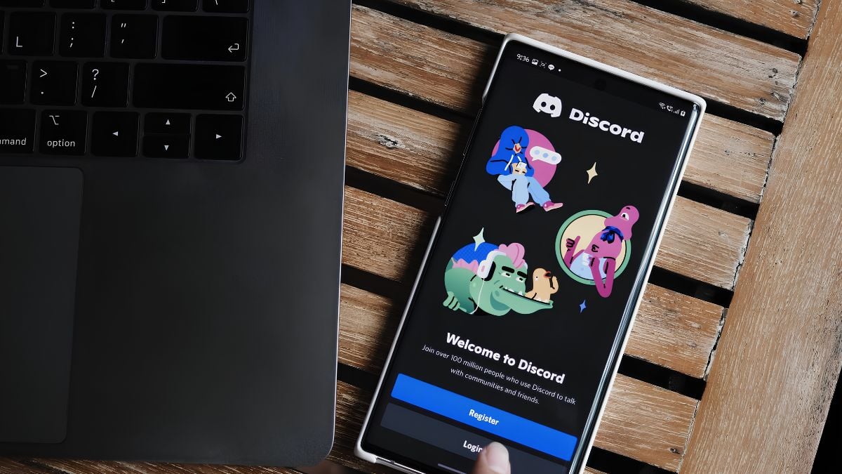 Imagem mostra um celular com o aplicativo Discord aberto sobre uma mesa de madeira, ao lado de um teclado e um cenário que remete a comunicação online. Adolescente teria usado Discord para vender material de abuso infantil em Santos.