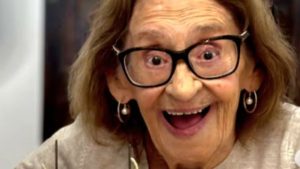 Laura Cardoso em close, sorrindo e usando óculos e brincos, em uma imagem que homenageia a atriz da dramaturgia brasileira.
