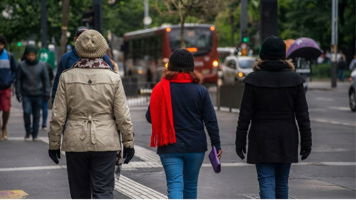 Pessoas caminhando na calçada com roupas de frio em São Paulo, enquanto ônibus e veículos passam ao fundo, sugerindo chegada de Ciclone extratropical em SP a partir de sexta com chuva e ventos fortes.