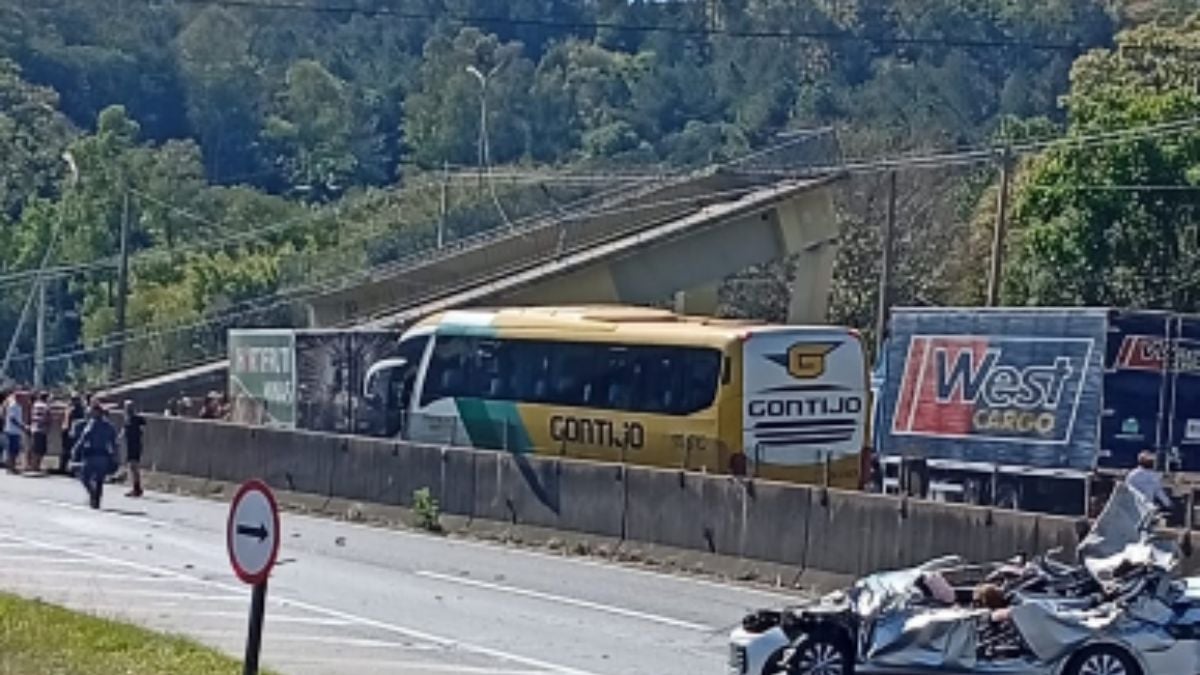 Acidente com caminhão na Fernão Dias: caminhões e destroços bloqueiam a rodovia após a queda de uma passarela, com carros e motocicletas danificados ao lado da pista.