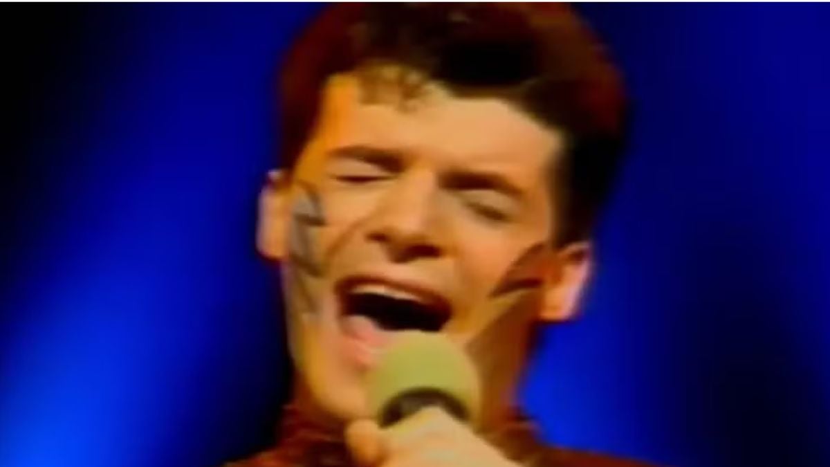 Carlos Cesare em cena, com expressão de canto e microfone ao fundo azul, lembrado como intérprete do Pablo do ‘Qual É a Música?’, em imagem de divulgação