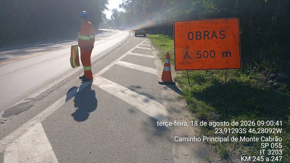 Operário sinaliza obras na estrada com cones e placa “OBRAS A 500 m” em trecho da SP-055, com aviso de trechos interditados Santos e Bertioga, na rota para Monte Cabrão.