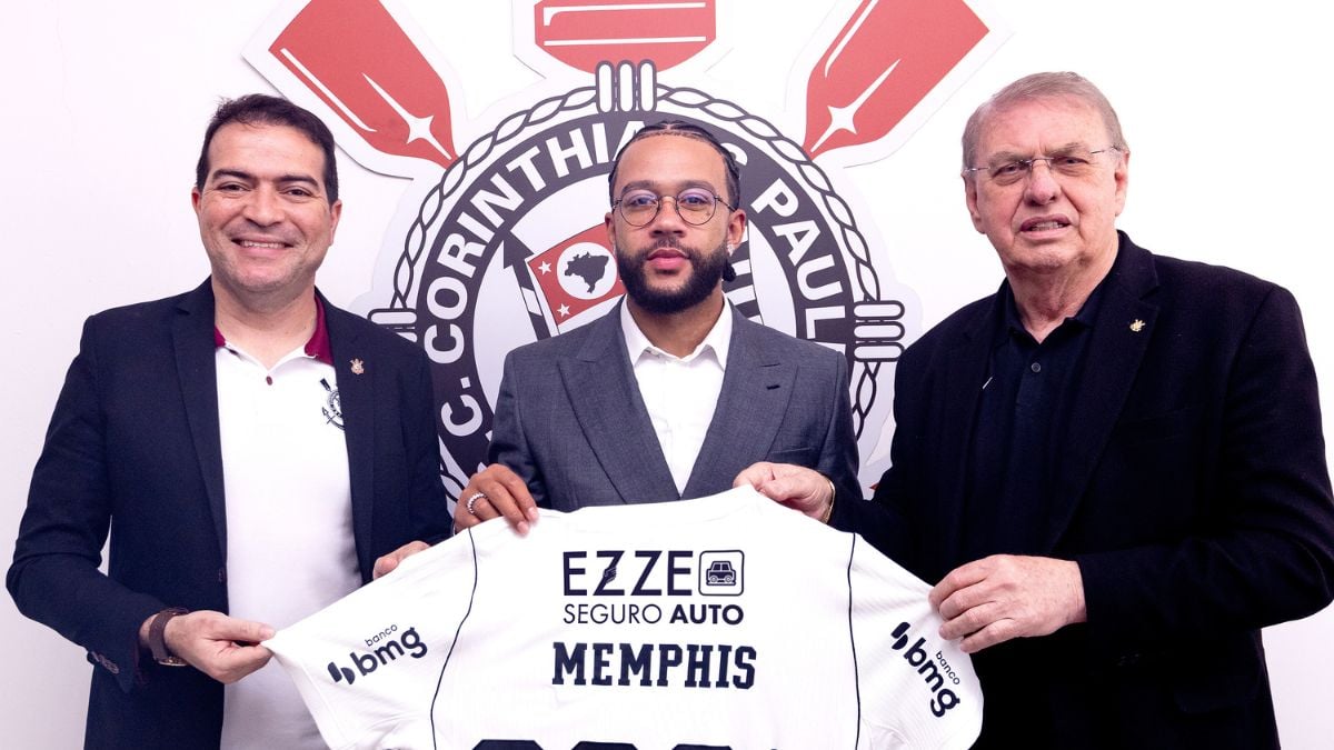 Memphis Depay renova com o Corinthians até 2028 e pode jogar na Libertadores: o jogador assina ao lado de dirigentes do clube, segurando uma camisa branca com o nome Memphis.