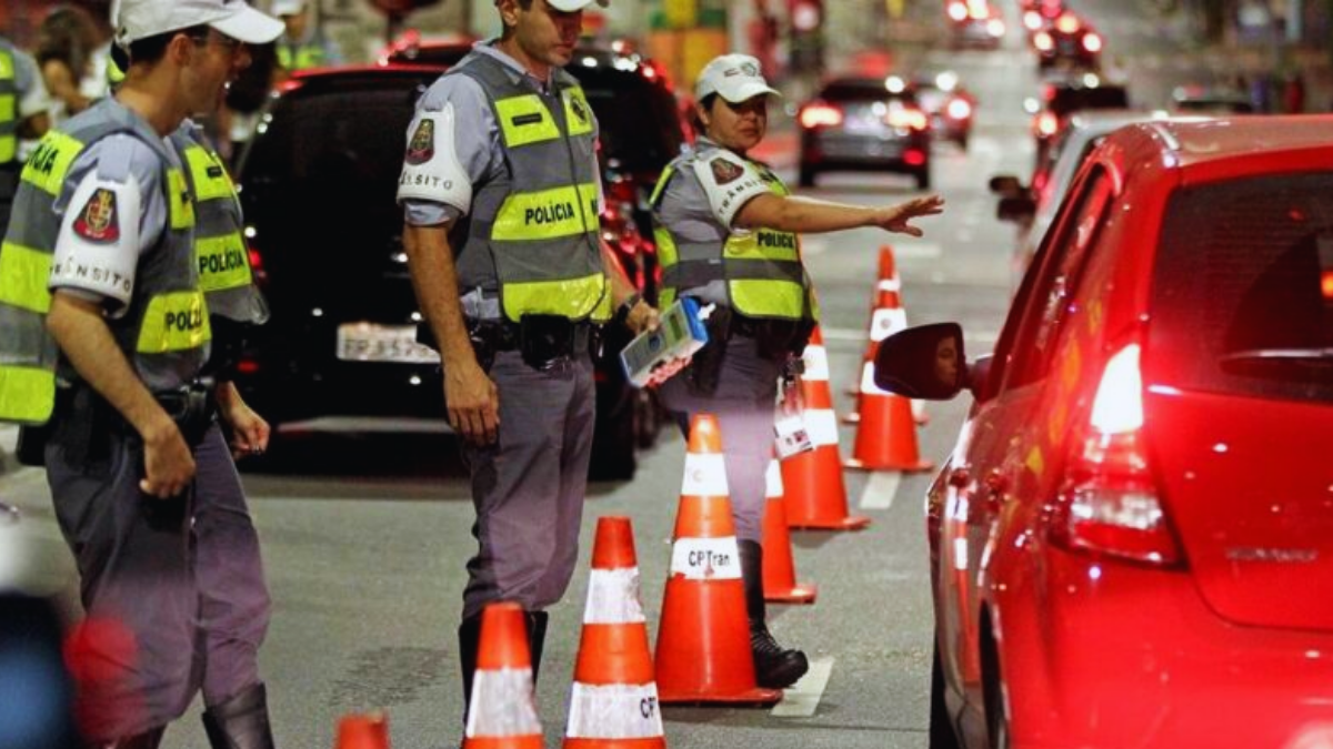 Drogômetro na Lei Seca com agentes de polícia em fiscalização na via, ao lado de cones e carros, em contexto de detecção de substâncias proibidas