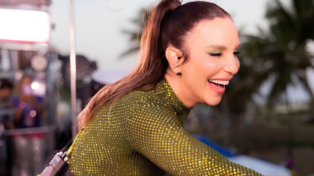 Ivete Sangalo em apresentação no palco, sorrindo e cantando durante o Rock in Rio 2026, com figurino brilhante verde e cenário de festival ao fundo.