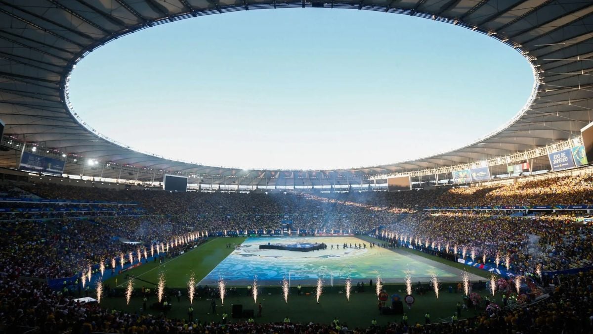 Copa do Mundo Feminina 2027: estádio lotado com campo de futebol visto de arquibancadas, equipes alinhadas e iluminação para a cerimônia de abertura.