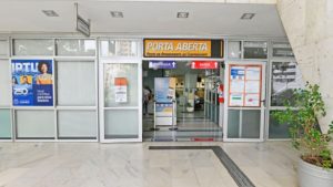 Entrada de prédio com faixa “PORTA ABERTA”, placas de orientação de entrada e saída e painel informativo, remetendo ao Feirão do Refis em Campinas com descontos em juros e multas do ISSQN.