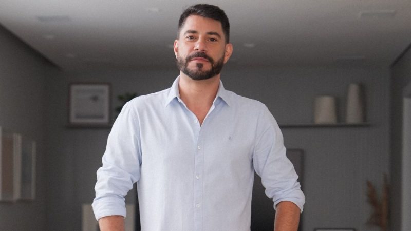 Evaristo Costa em foto promocional, vestindo camisa social branca, falando para a câmera em ambiente interno, com expressão séria ao anunciar conteúdo adulto.