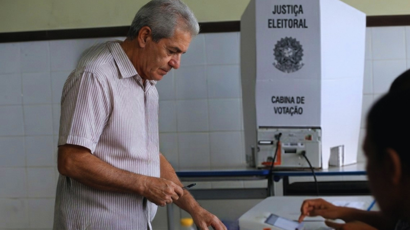 Eleitores com mais de 60 anos em votação: homem idoso preenchendo cédula em cabine de votação na Justiça Eleitoral durante as eleições 2026.