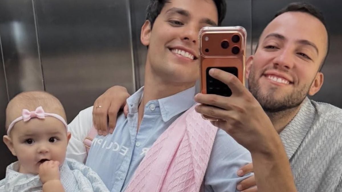 Lucas Rangel e Lucas Bley posam com a filha pela primeira vez na praia em Santos, em foto de elevador com celular, sorrindo e abraçando o bebê.