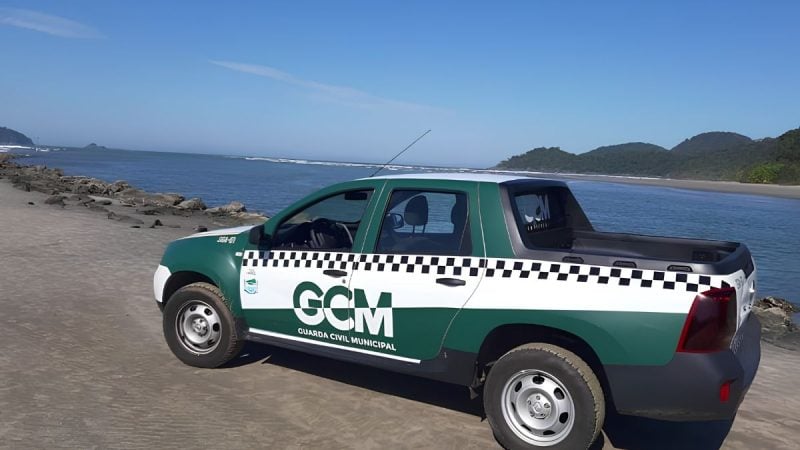 Mulher chama GCM de macaca em Peruíbe: Veículo da GCM (Guarda Civil Municipal) estacionado na orla de Peruíbe, com o texto GCM e uma faixa preta e branca na lateral, em cenário de praia ao fundo.