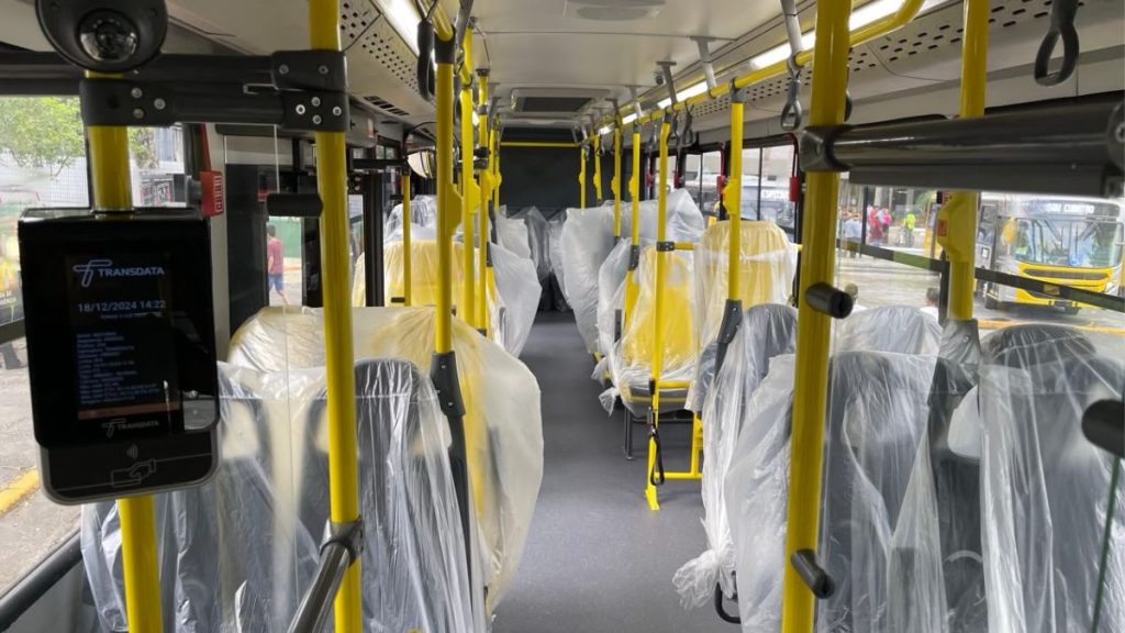 Interior de um ônibus coletivo com bancos cobertos e barras amarelas, mostrando atendimento da Sou Transportes com frota de 320 ônibus para transporte em Campinas durante a crise do setor.