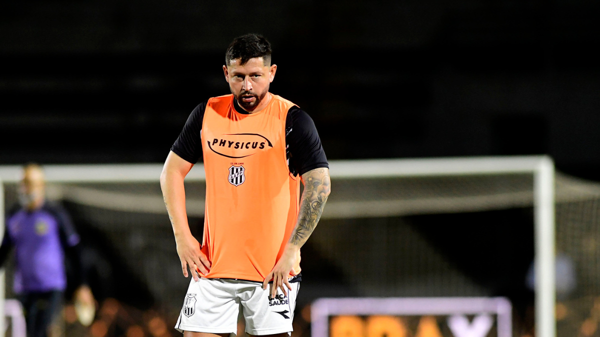 Elvis em campo usando colete laranja do Santos, segurando as costas e olhando para a torcida em partida sob a luz do estádio; após lesão, deixa recado para a Ponte: “Nossa história não acabará assim”.