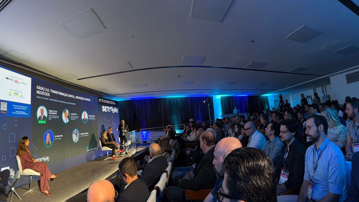 Rádio 3.0 em evento, com público reunido em uma sala de conferências e painel de apresentações em telões, destacando a transformação do rádio e a necessidade de entender essa evolução.