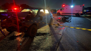 motociclista de 22 anos morre em Cosmópolis: Acidente de trânsito à noite com carro e motocicleta, viatura e ambulância ao fundo; na pista há moto caída e faixas amarelas de isolamento próximo a Cosmópolis.