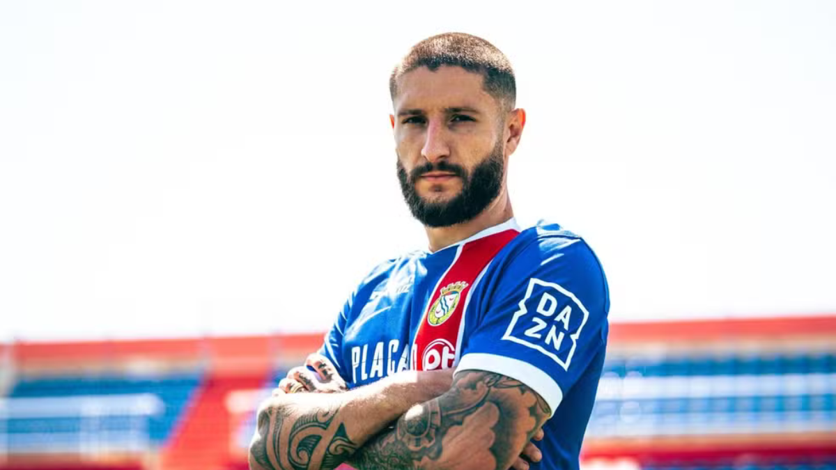 Zé Rafael, jogador em foto de uniforme azul do Santos, aparece em campo com braços cruzados e olhar firme em destaque; contexto sobre sua saída do clube.