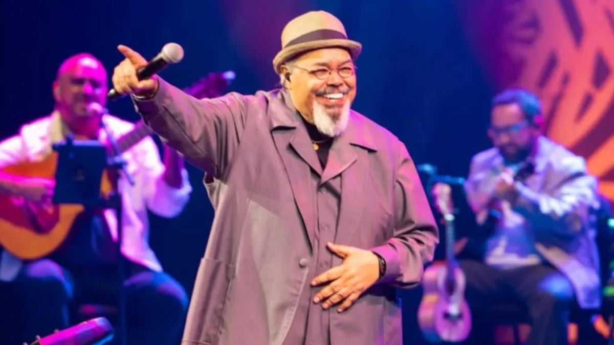 Jorge Aragão no Santos Carnaval 2027: cantor aparece no palco durante a festa de lançamento do evento, com braço estendido e microfone, em show ao vivo com banda ao fundo.